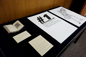 Overview of materials on display, showing a cradled book and two pages from a very large set of prints.