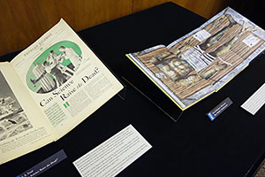 Overview of materials on display, showing a cradled book and two pages from a very large set of prints.